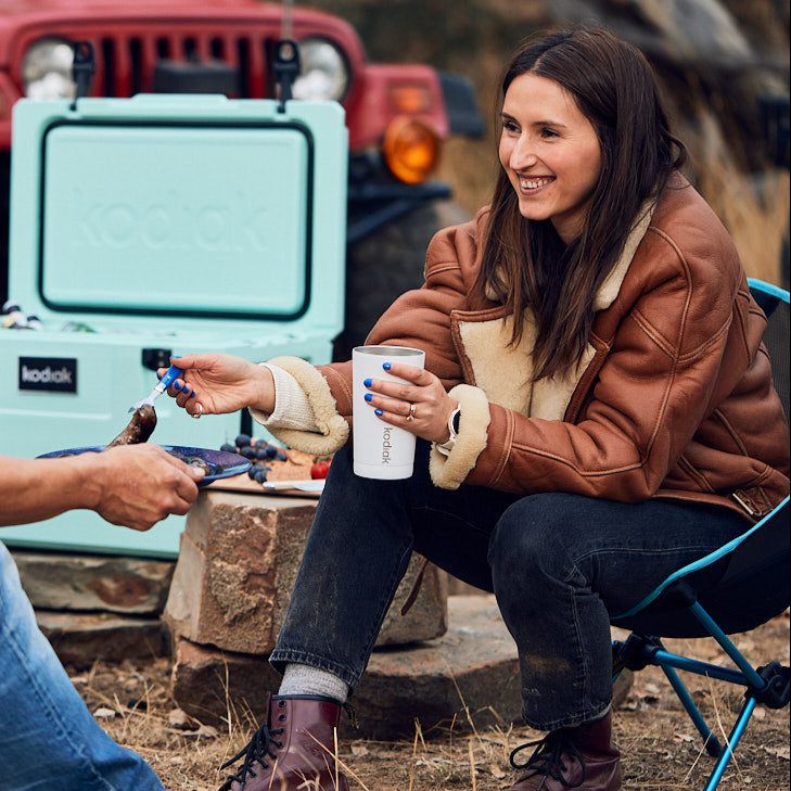 Kodiak 473 Tumbler White 473ml Insulated Stainless Steel Drinkware held by woman at outdoor campsite with cooler